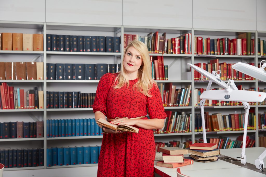 Portrait of Vikki Hawkins, the Second World War Curator at Imperial War Museums. Vikki is pictured in the museum’s library room, holding a book.