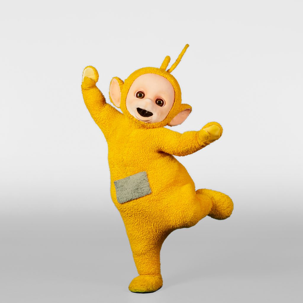 Laa-Laa is posing in a white studio with hands in the hair, and one foot balanced above the ground. 