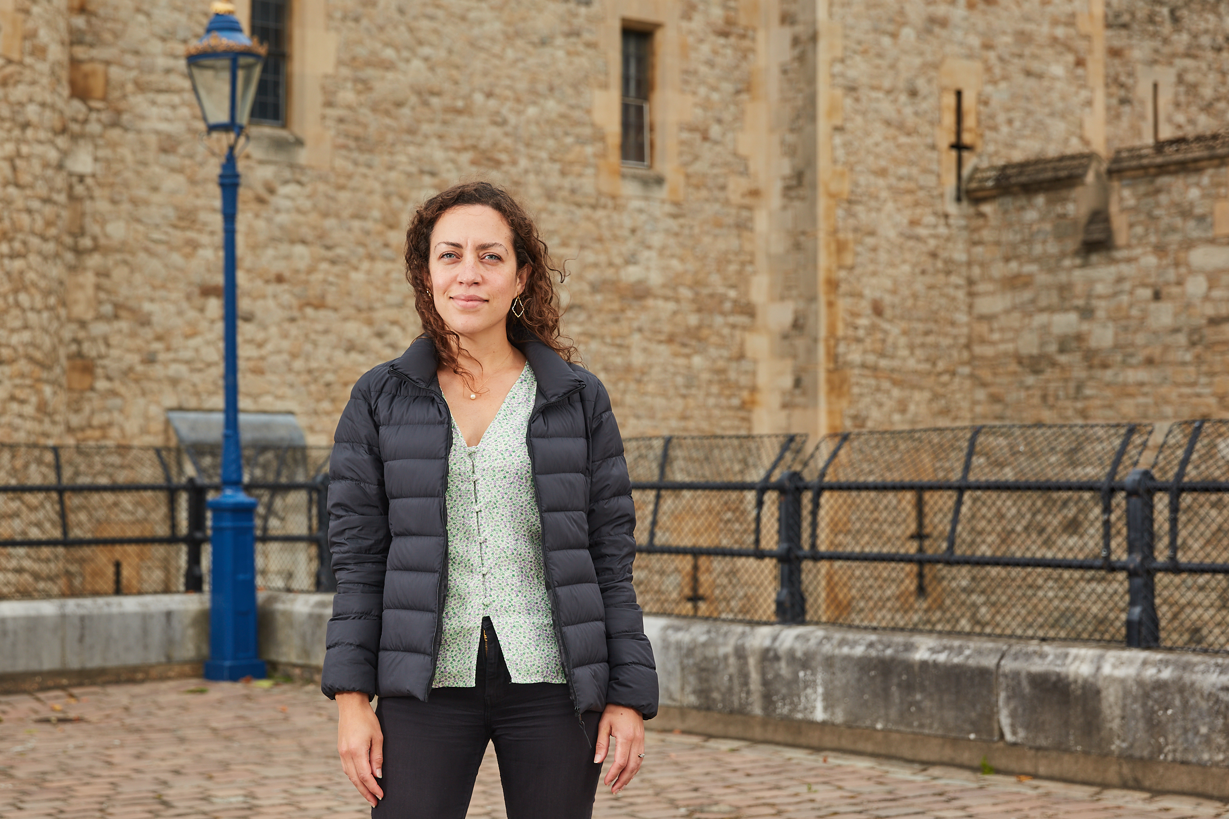 Portrait of Dr Misha Ewen, Curator of Inclusive History of Historic Royal Palaces, standing in front of the Tower of London. 